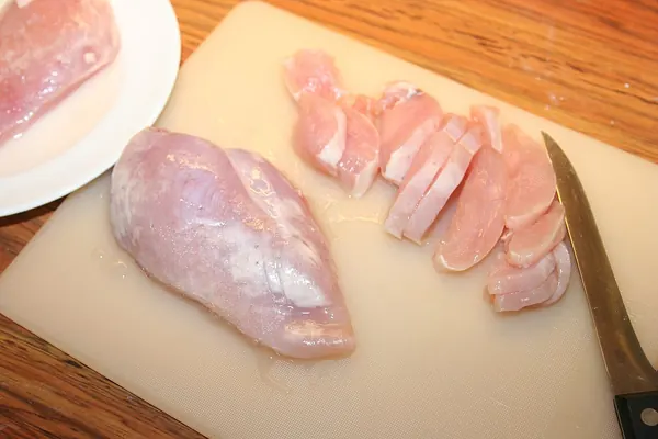Raw chicken breast on a cutting board, partly sliced