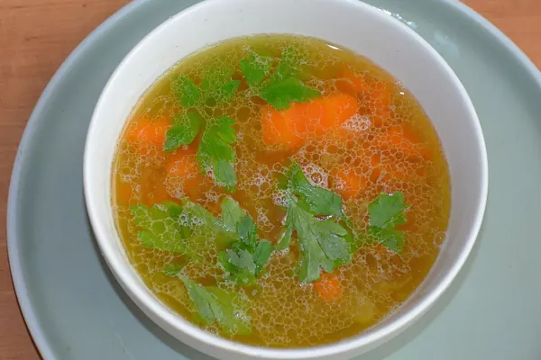 A bowl of bone broth with carrot and parsley